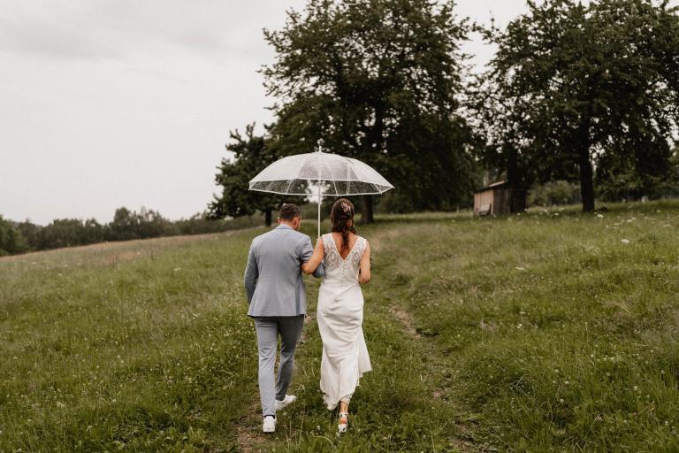 Brautpaar von hinten mit Schirm im Regen