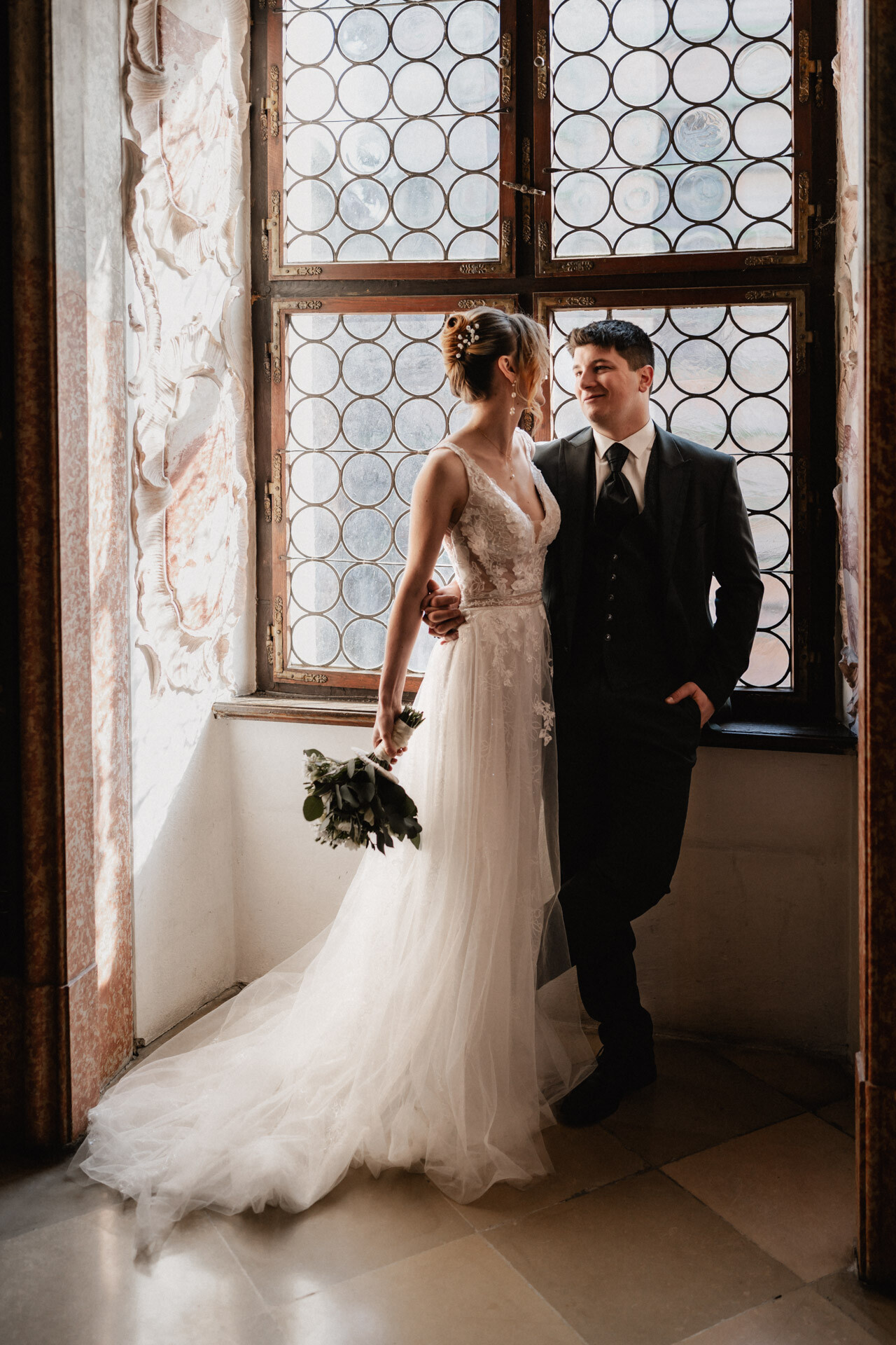 Brautpaar steht an Fenster, aufgenommen von Hochzeitsfotograf Ludwigsburg