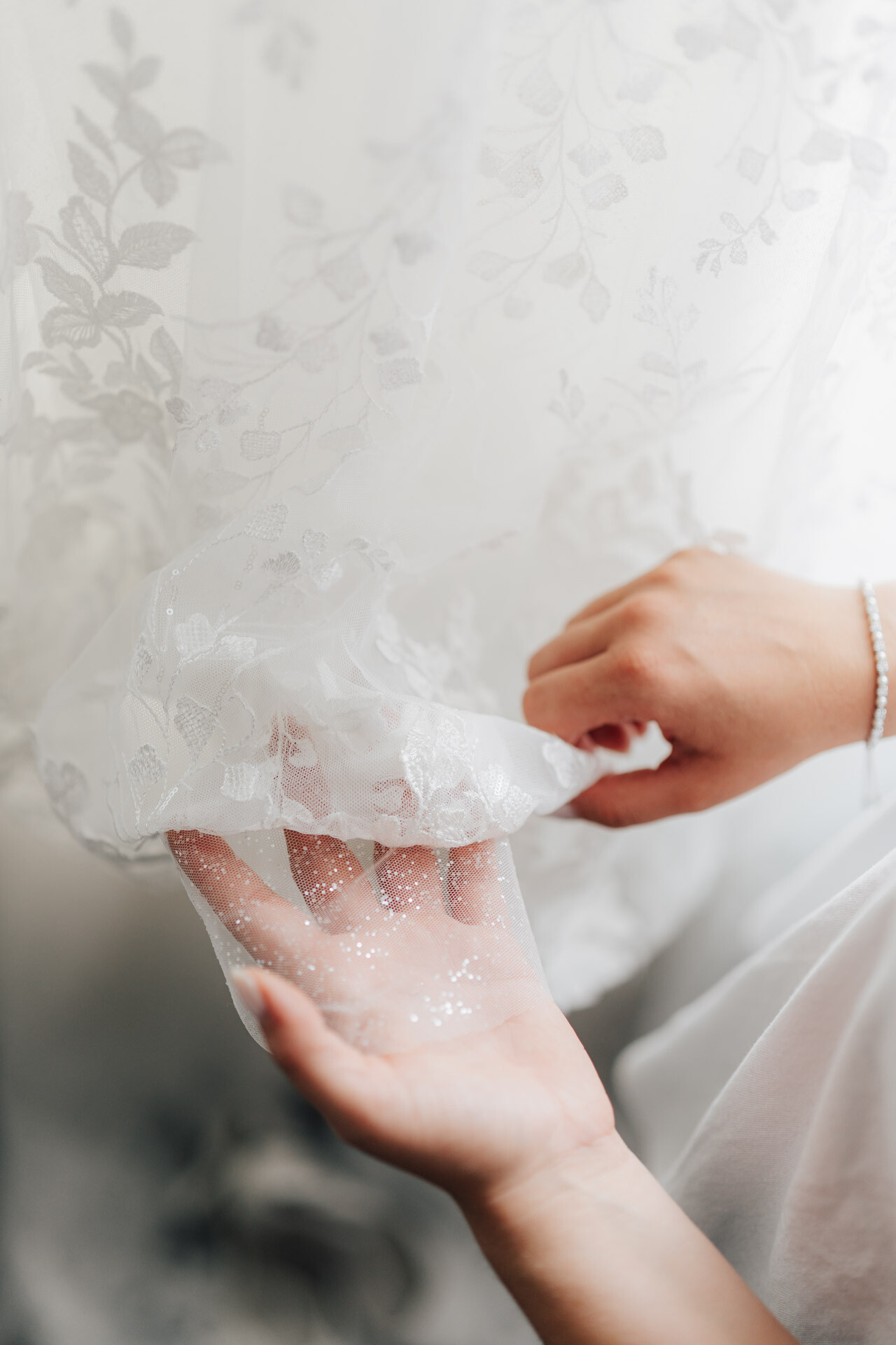 Eine Nahaufnahme der Hände einer Person, die sanft einen durchsichtigen, floral gemusterten weißen Stoff mit Glitzer auf der Handfläche hält. Die weiche, zarte Szene erinnert an das verträumte Ambiente einer Gewächshaus-Hochzeit in Leinfelden-Echterdingen.