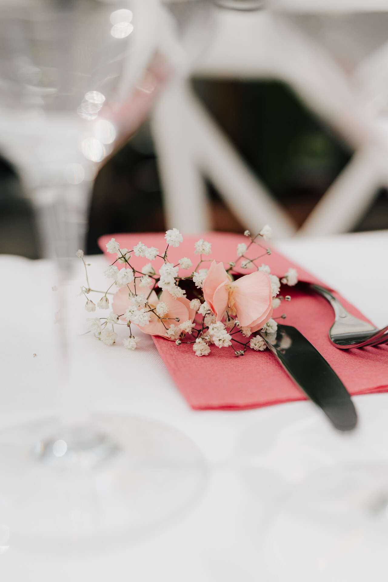 Eine rosafarbene Serviette auf einem weißen Tisch hält ein schwarzes Messer und eine schwarze Gabel, die mit hellrosa Blumen und Babyatem verziert sind. So entsteht eine elegante Tischdekoration, die perfekt für eine Gewächshaus-Hochzeit im Plangarten Leinfelden-Echterdingen ist.