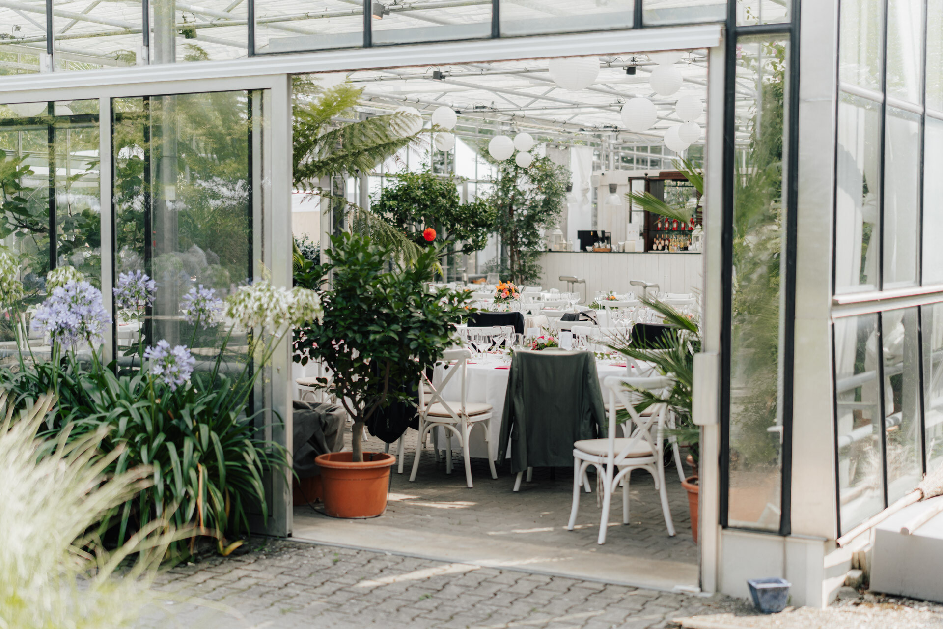 Eine Glaswand mit Tischen und Stühlen schafft einen reizvollen Rahmen im Gewächshaus Plangarten, perfekt für eine Hochzeit in Leinfelden-Echterdingen.