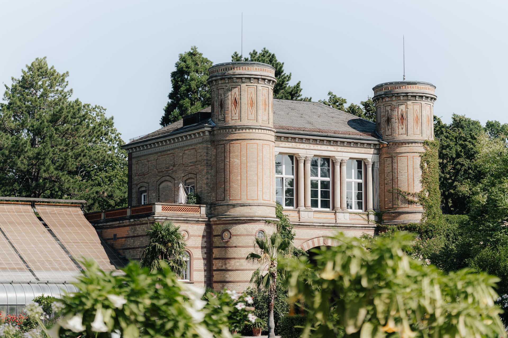 Ein historisches Backsteingebäude mit zwei Rundtürmen und Rundbogenfenstern, umgeben von Grün und Bäumen unter freiem Himmel - ein zauberhafter Hochzeitsort bei Tante Polly in Karlsruhe.