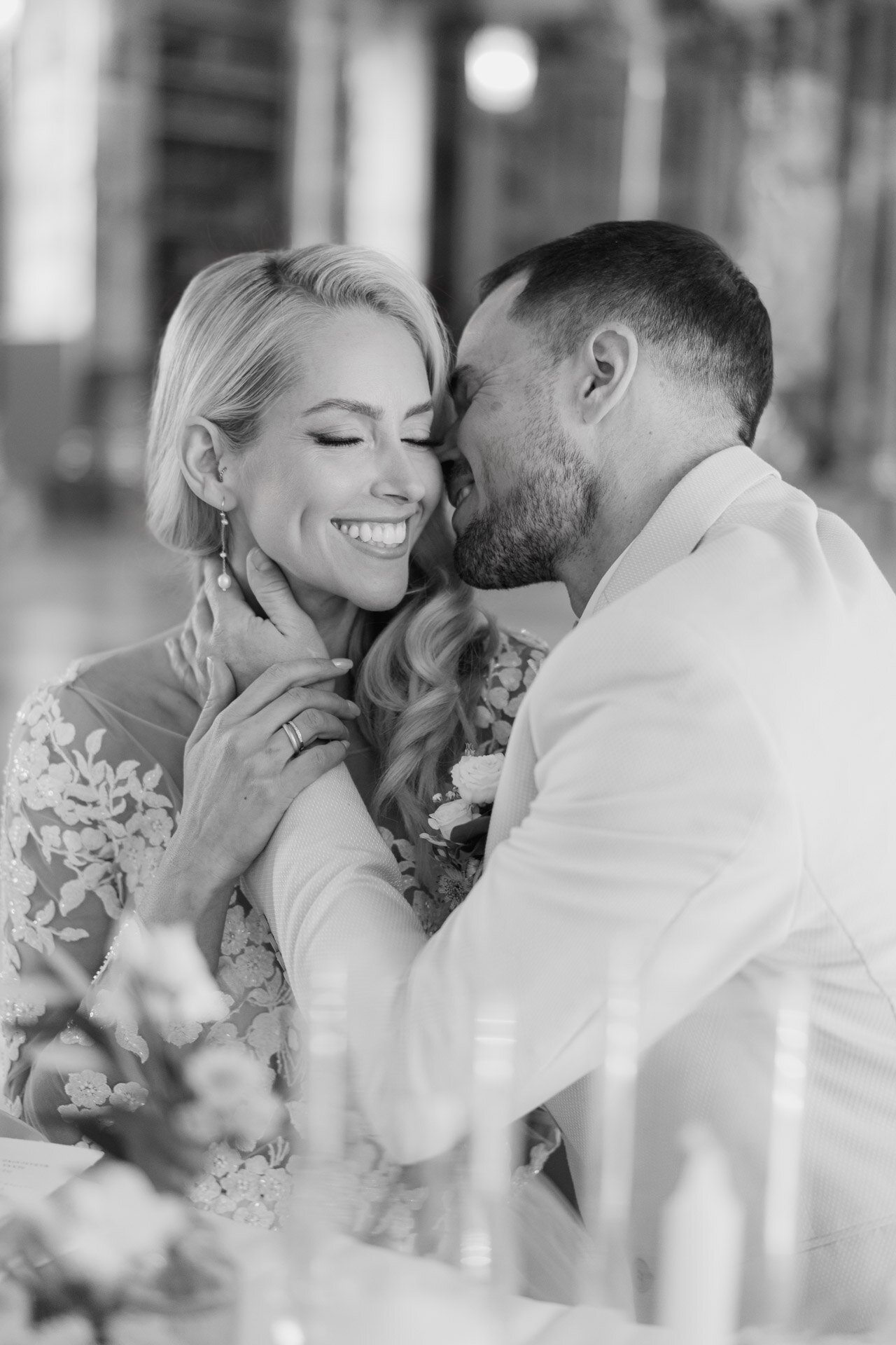 Ein Mann mit hellbraunem Haar und einem Bart sitzt auf einem grauen Sofa und lächelt in die Kamera. Er trägt ein grünes Button-up-Hemd und eine dunkle Hose - vielleicht ein Hochzeitsfotograf Göppingen - während hinter ihm gerahmte Schwarz-Weiß-Fotos an der Wand hängen.