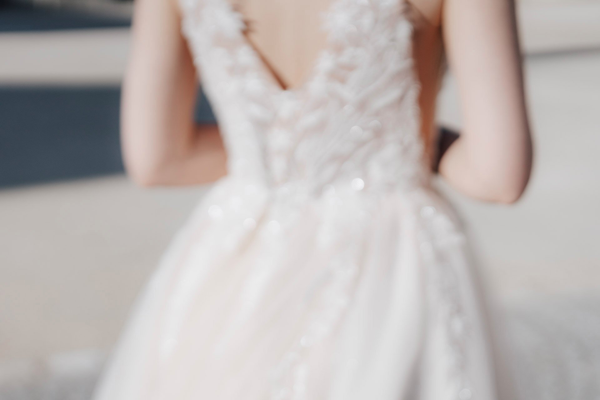 Ein Weichzeichnerbild, das den Rücken einer Person zeigt, die ein ärmelloses, spitzenbesetztes weißes Kleid, möglicherweise ein Hochzeitskleid, im Freien in hellem Sonnenlicht trägt - aufgenommen von einem Hochzeitsfotografen aus Pforzheim.