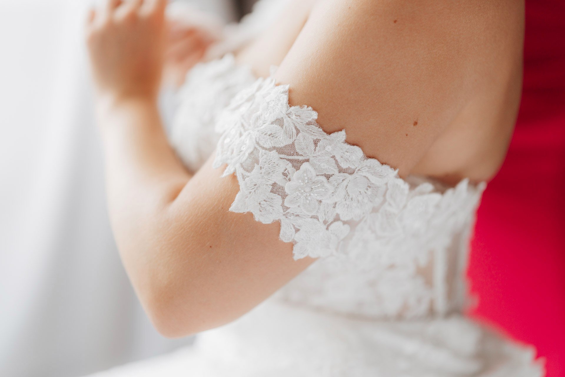 Nahaufnahme einer Person, die ein schulterfreies weißes Spitzenhochzeitskleid trägt, das ihre nackte Schulter und ihren Oberarm mit floralen Spitzendetails zeigt - die perfekte Inspiration für jeden Hochzeitsfotografen Pforzheim.