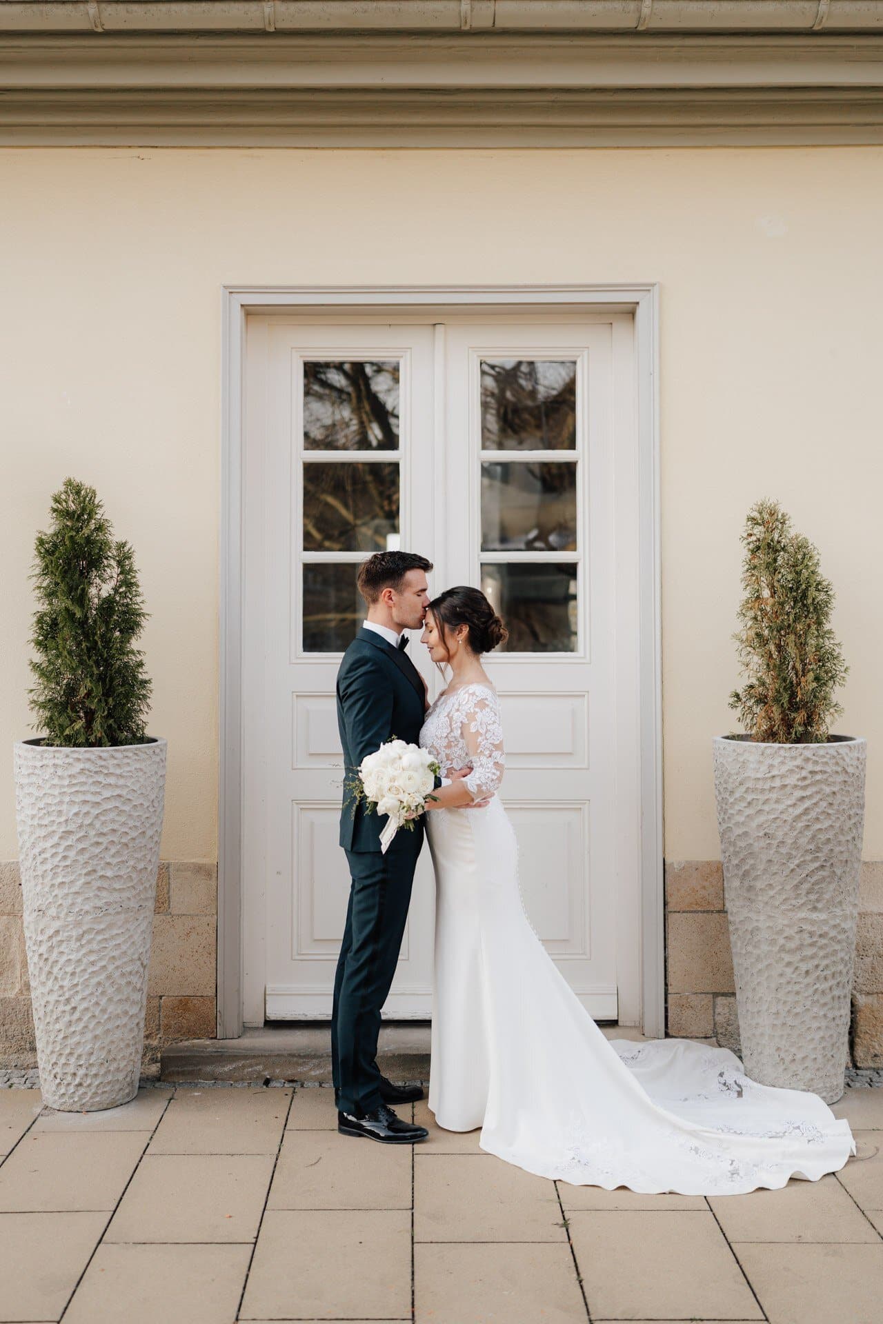 Brautpaar steht sich gegenüber vor einer hellen Tür neben zwischen Pflanzenkübeln für Hochzeitsfotograf Stuttgart.